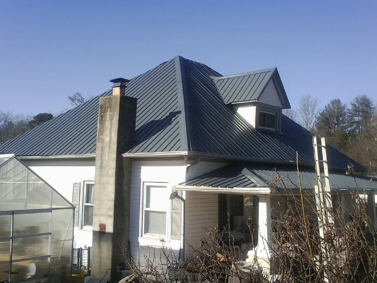 Dark blue standing seam metal roof on a white farmhouse with dormer — Slate & Tile Roof Repair by Roofing Brothers in Rigby