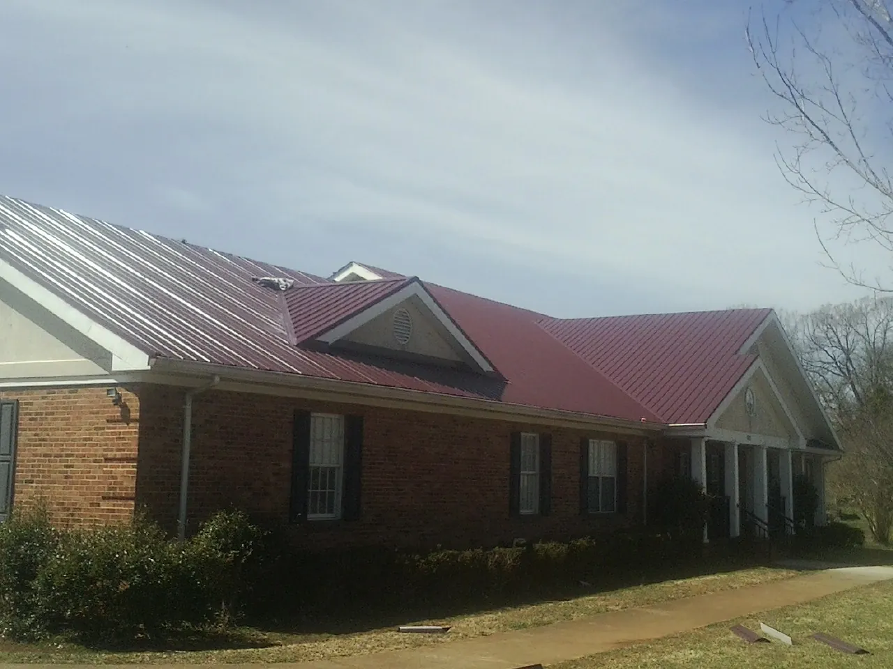 Red metal roof with gabled entries on a long brick building, from a Hail Damage Roof Repair job in Rigby