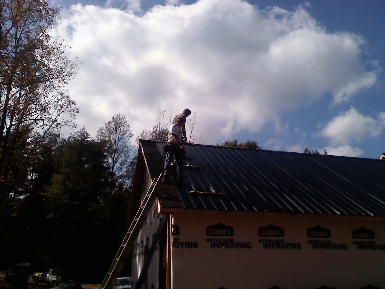 Roofer fastening dark metal panels high against a cloudy sky, from a Roof Inspection job in Rigby