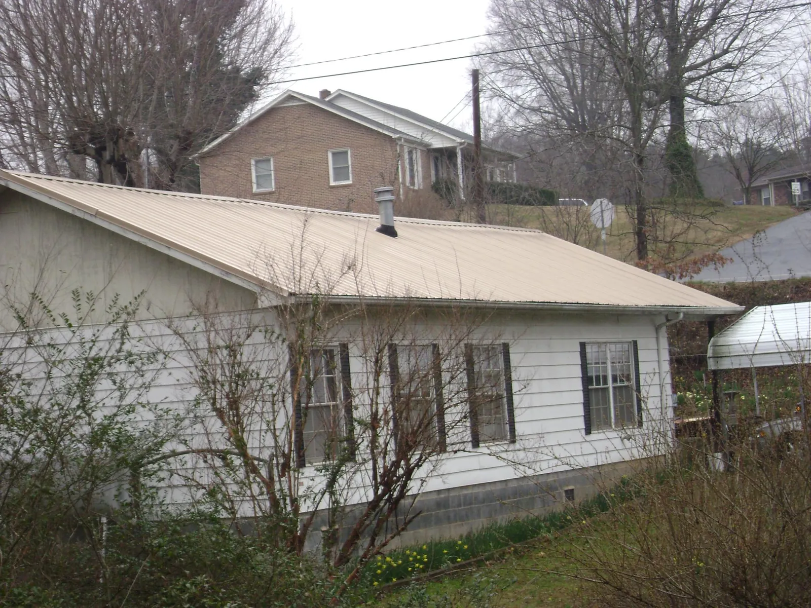 Tan metal roof on a white sided house set into a hillside — Commercial Roofing by Roofing Brothers in Rigby
